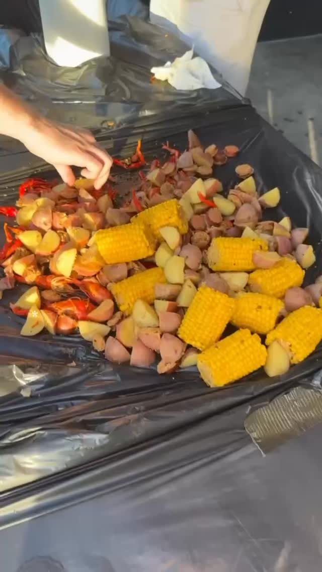 Seafood boil with corn, potatoes, and sausage spread on a black plastic tablecloth.