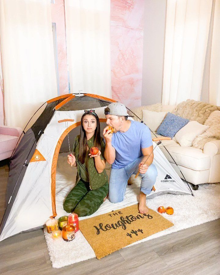 Couple sitting inside a camping tent set up in a living room eating fruit.