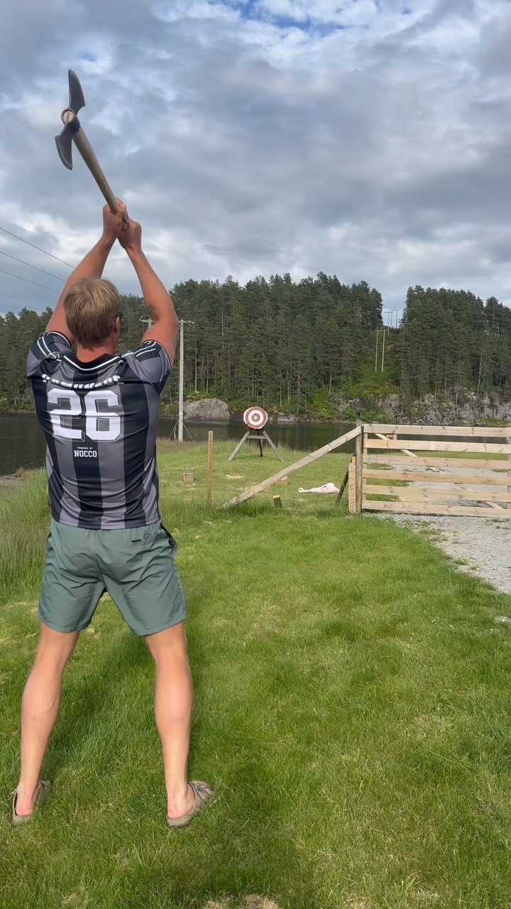 Man in sports jersey preparing to throw an axe at a target outdoors.