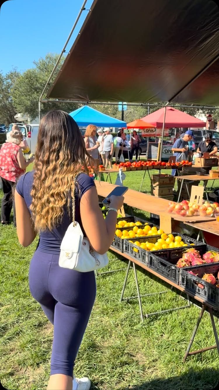 Woman in navy athletic wear browsing fresh produce at an outdoor farmers market.