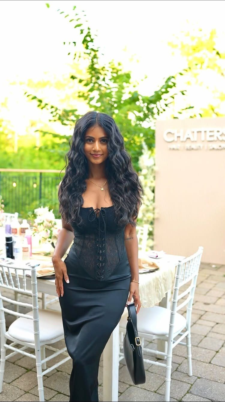 Woman in a black figure-flattering maxi dress standing by a white dinner table.