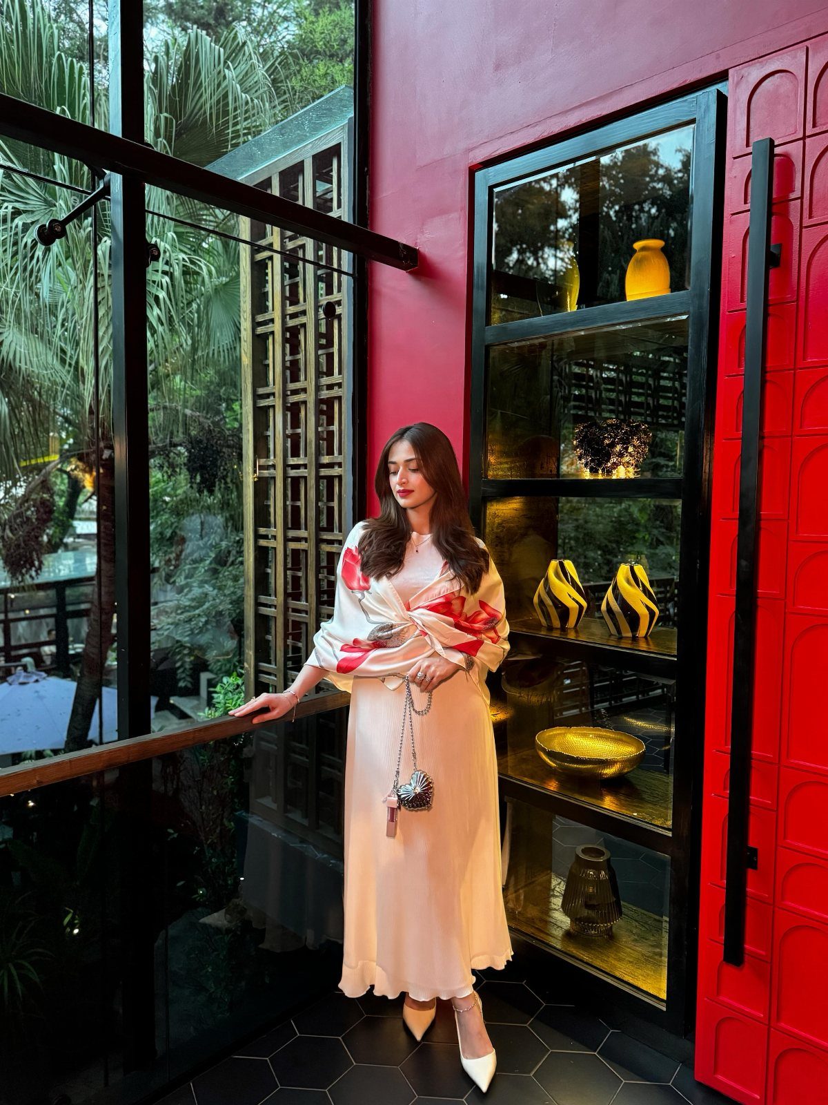 Woman in a cream midi dress and matching wrap standing by red walls.