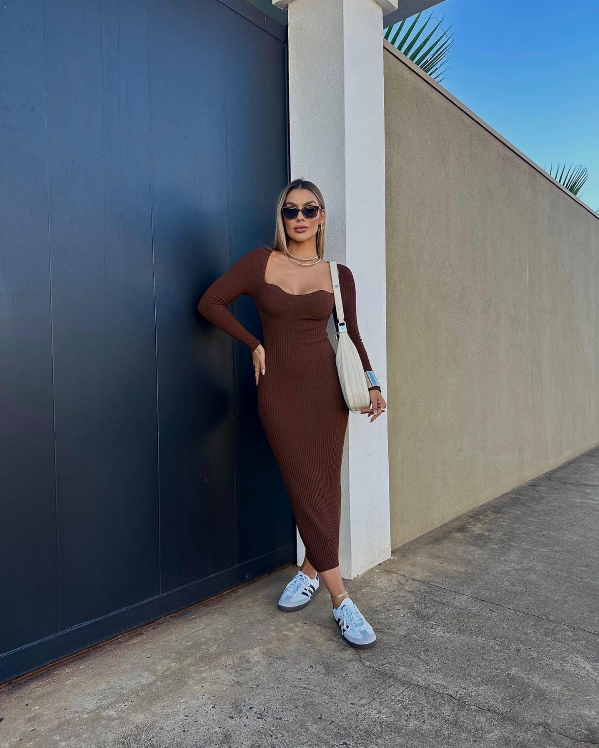Woman in a brown ribbed midi dress and white sneakers posing outdoors.