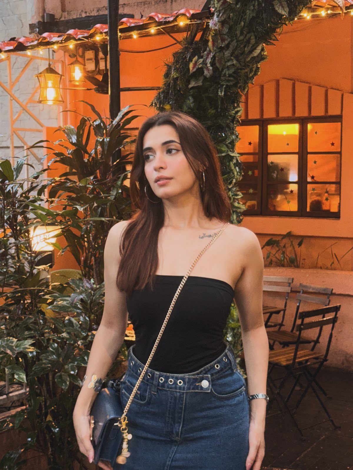Woman in black strapless top and high-waisted blue jeans standing in outdoor patio