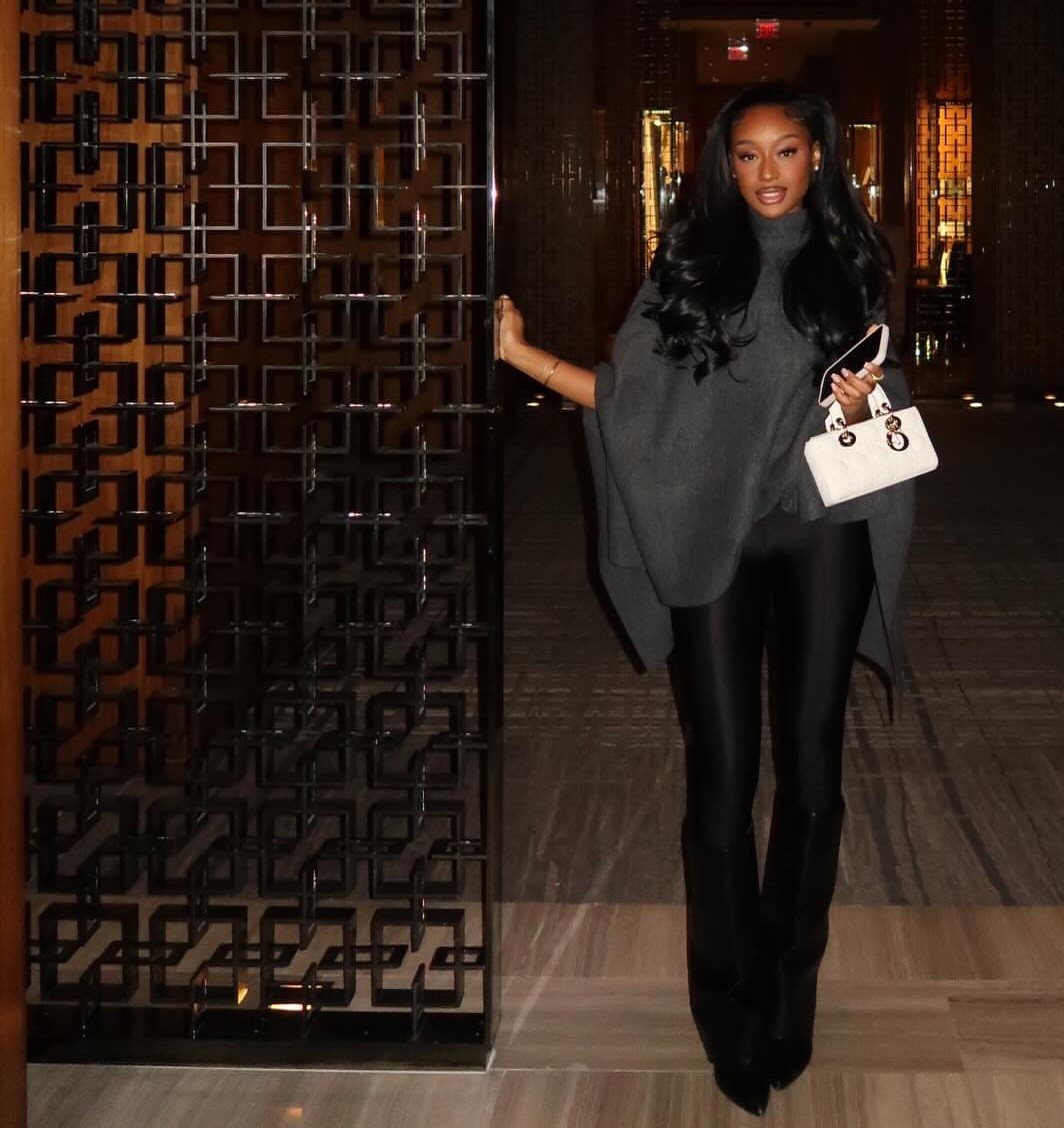 Woman wearing a grey oversized sweater, black leather leggings, and black heeled boots.