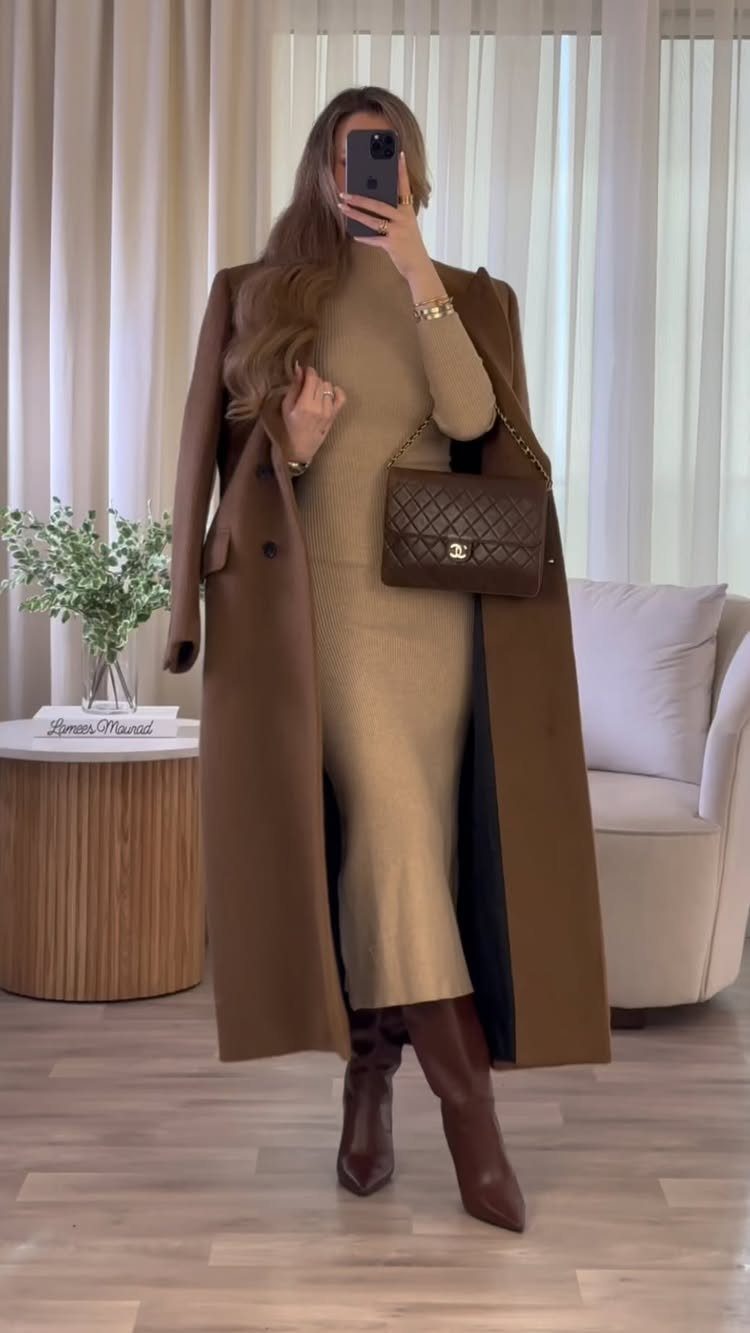 Woman in a fitted beige knit dress and long brown wool coat with boots.