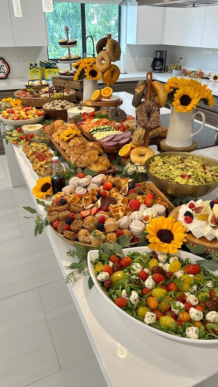 Brunch food spread on a white counter with waffles, croissants, and yellow sunflowers.