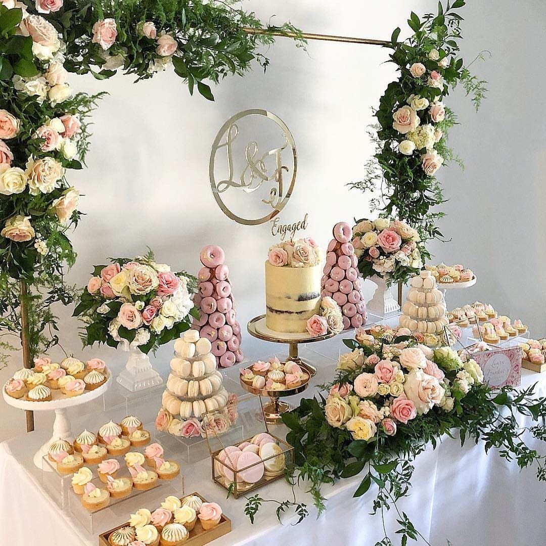 Dessert table with cake, donuts, and macarons decorated with pink and white roses.
