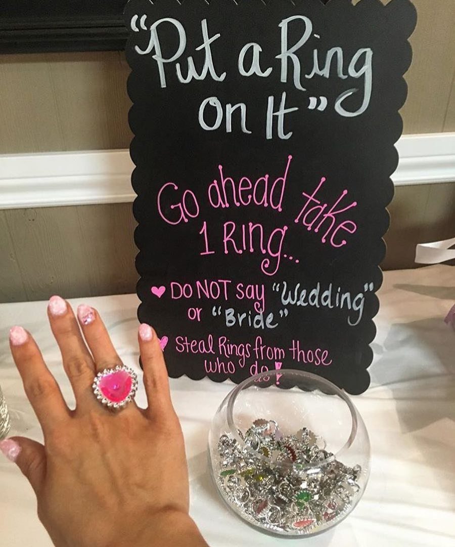 Hand wearing a pink heart ring next to a bowl of rings and sign.