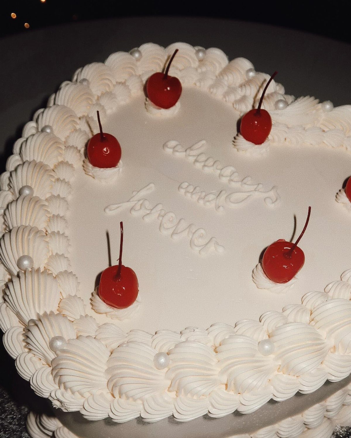Heart-shaped white cake decorated with red cherries and always and forever icing text
