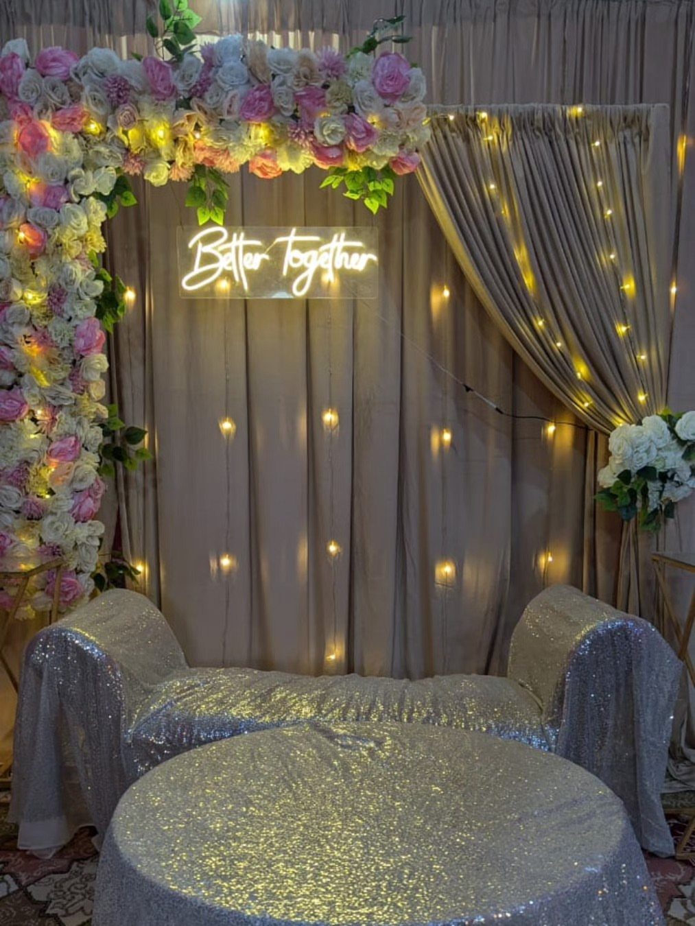 Silver sequined furniture and floral arch with a Better Together neon sign backdrop.