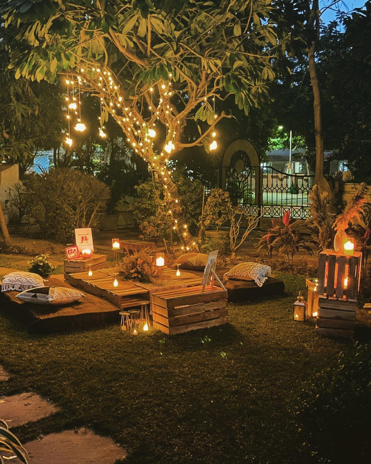 Cozy outdoor garden seating with wooden pallets, cushions, and fairy lights in a tree