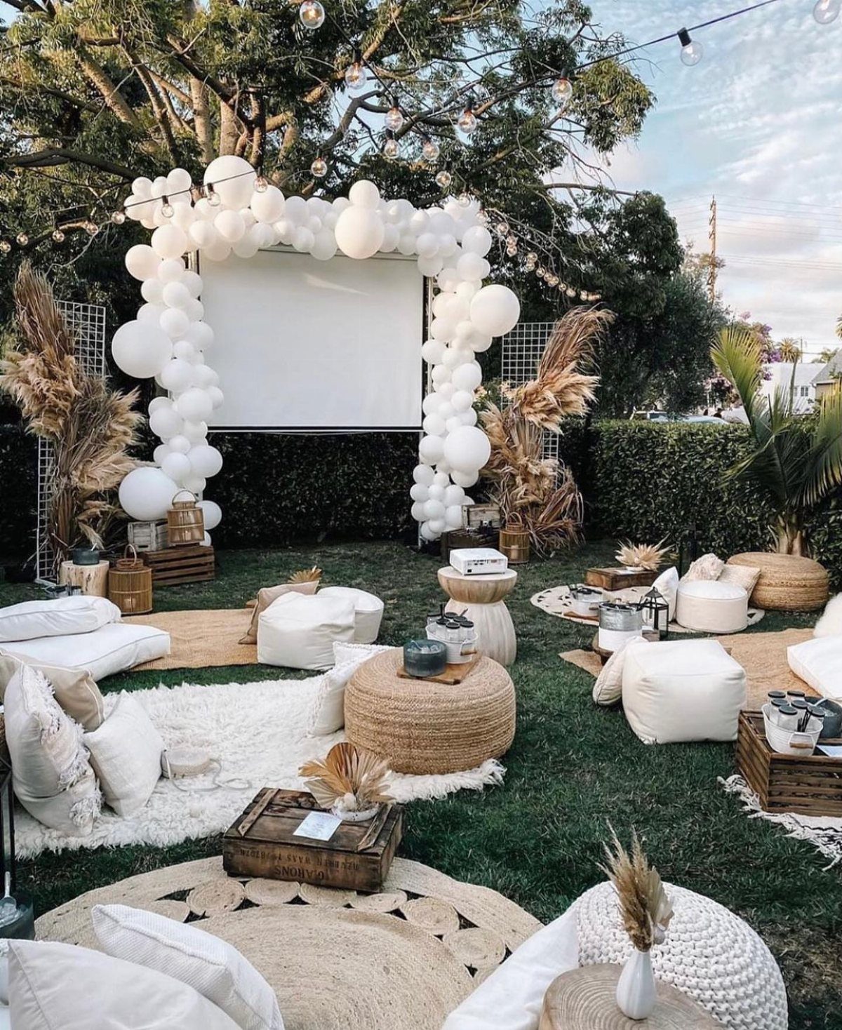 Outdoor movie screening setup with a white projection screen, balloon arch, and cozy seating.