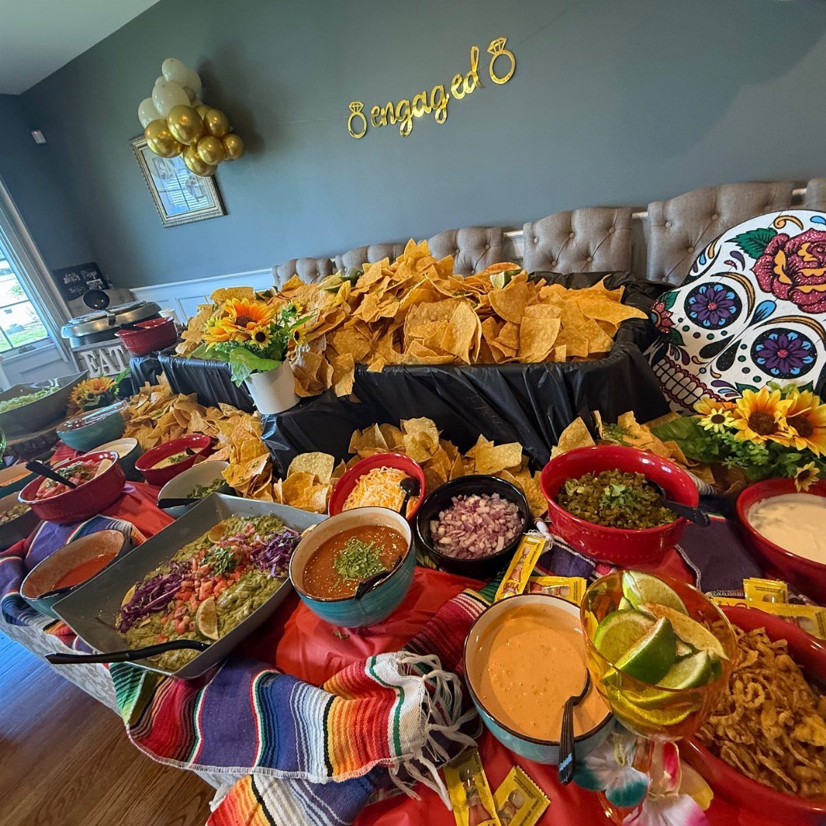 Taco bar spread with tortilla chips, dips, and a gold Engaged wall sign.