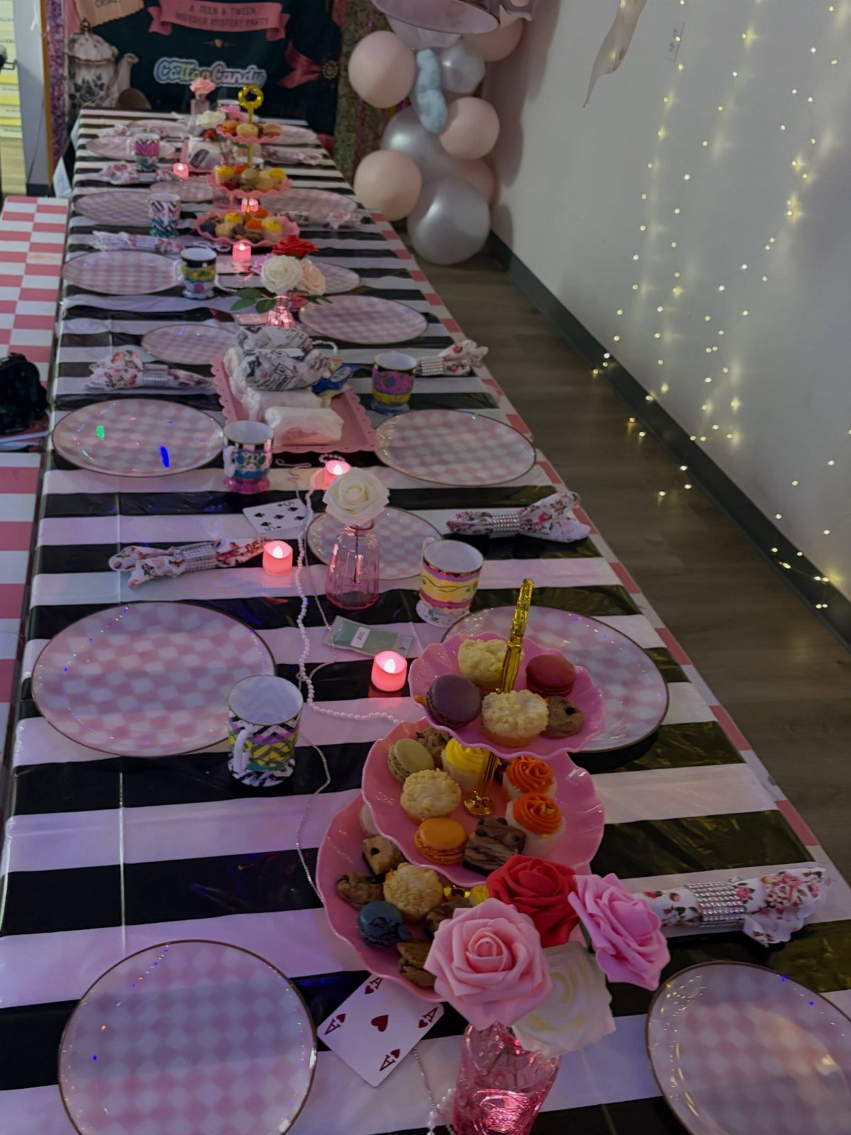 Party table with striped tablecloth, pink plates, macarons, and floral decorations.