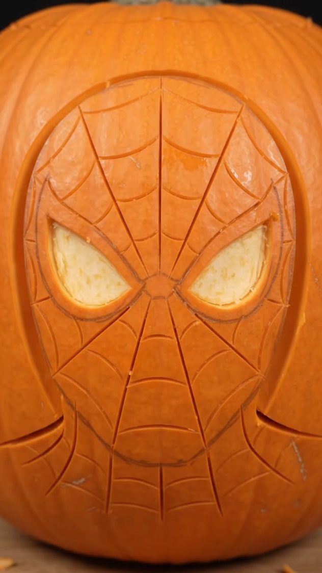 Orange pumpkin carved with a detailed Spider-Man mask and web pattern.