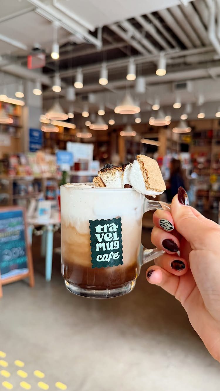 Layered coffee drink with toasted marshmallows held in a cozy cafe setting
