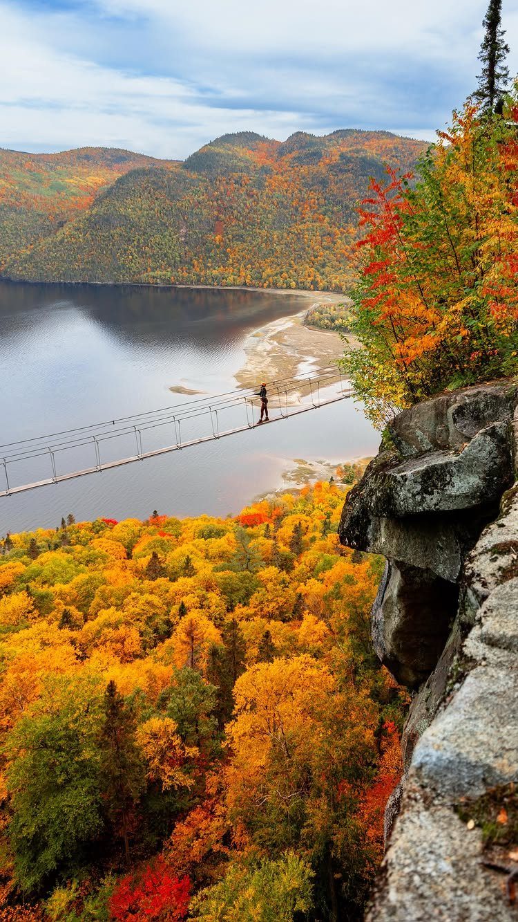 Person on a suspension bridge overlooking a lake and colorful autumn forest mountains.