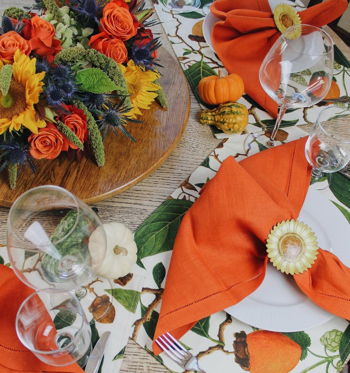 Autumn dinner table setting with orange napkins, small pumpkins, and floral centerpieces.