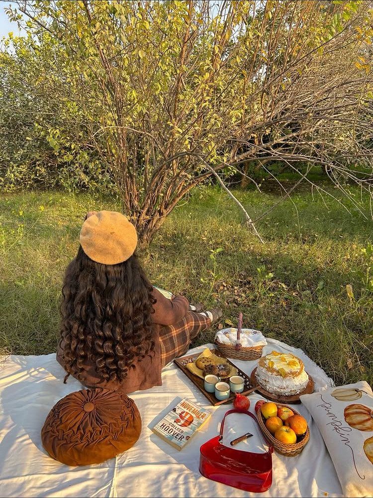 Woman in a beret sitting on a picnic blanket with food in autumn