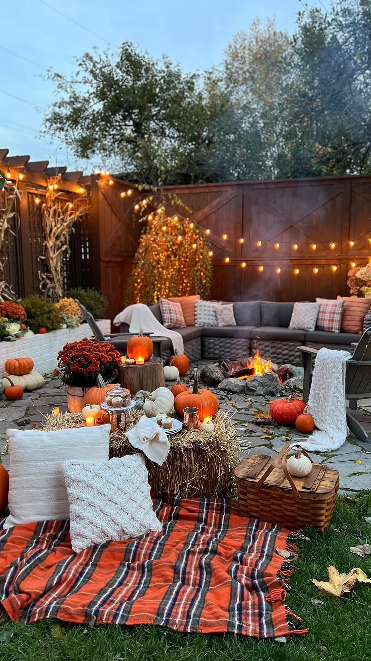 Outdoor fire pit area decorated with pumpkins, hay bales, and cozy blankets at dusk.