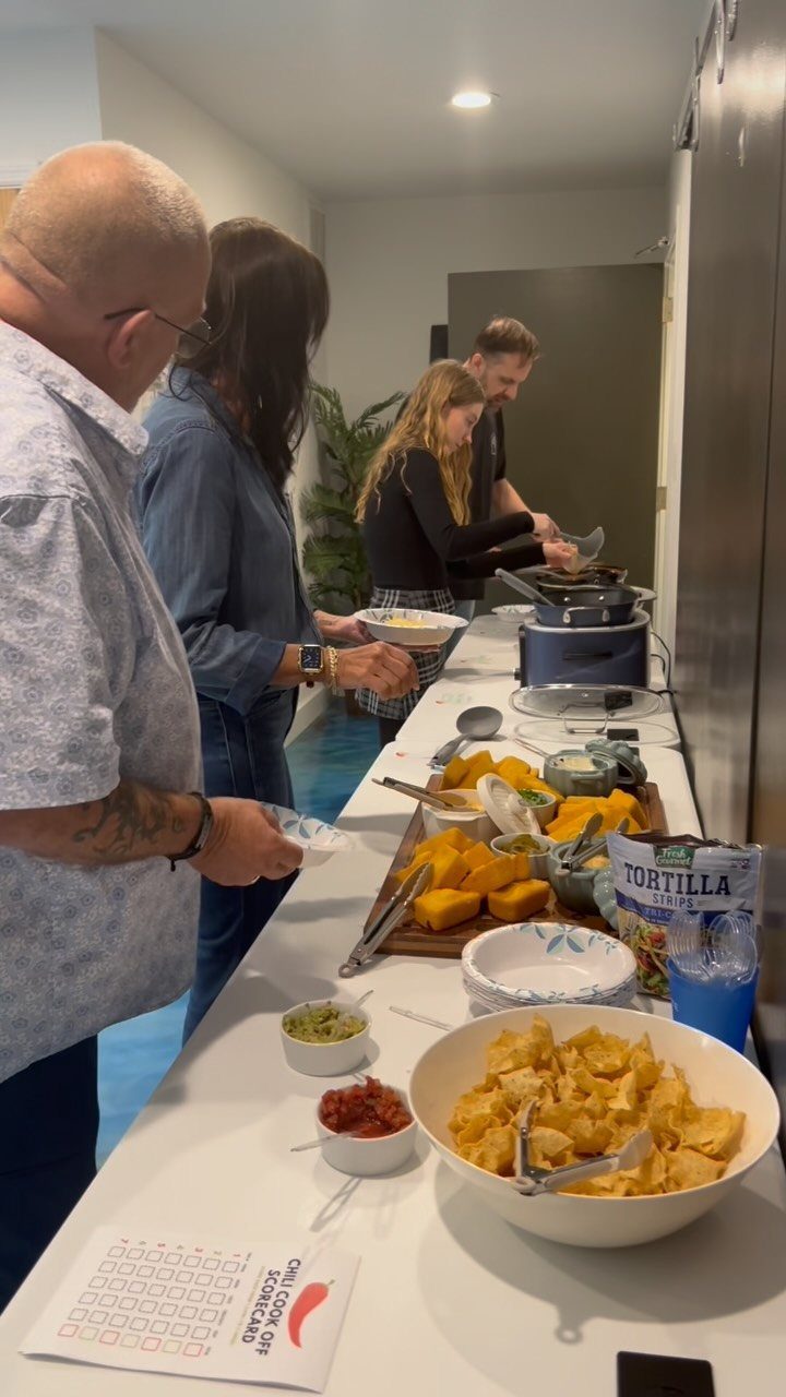 Adults gathering around a kitchen counter with chili and a score card.