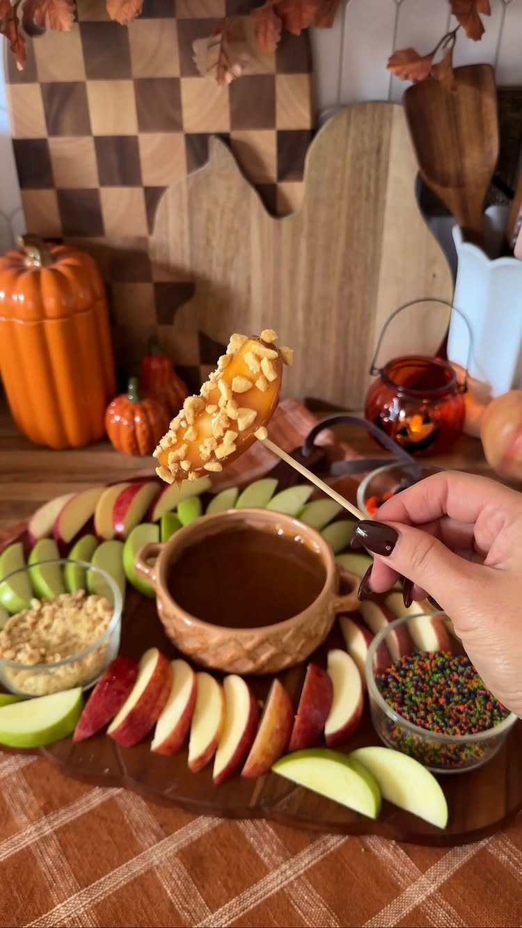 Caramel apple platter with sliced apples, dipping sauce, and autumn decorations.