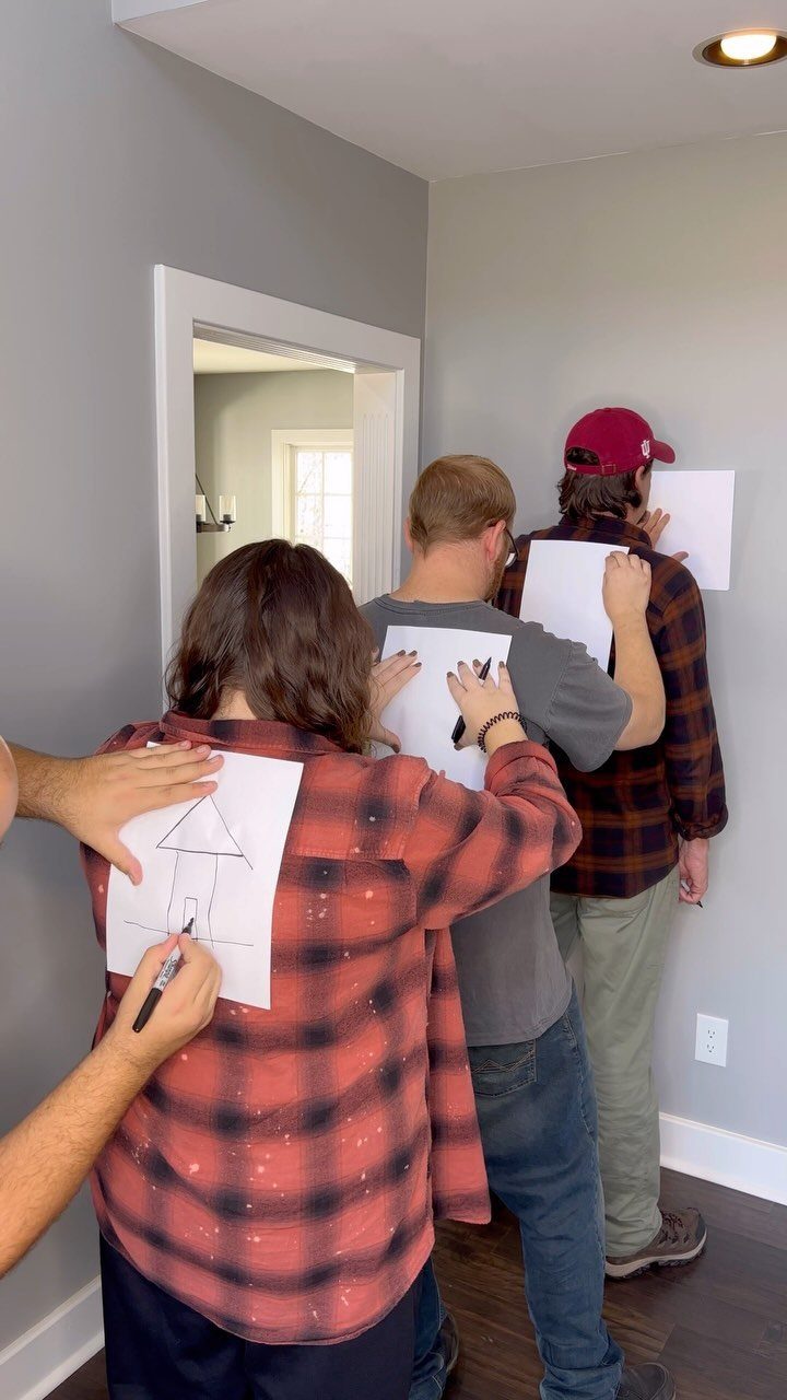 People playing a drawing game by sketching on papers taped to each other's backs.