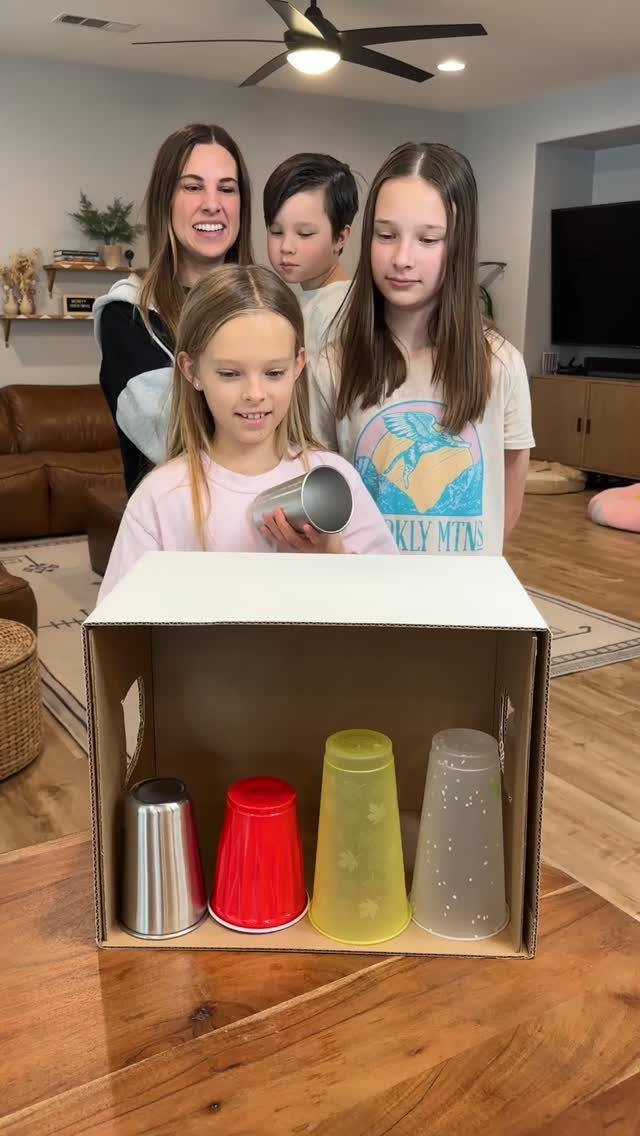 Family playing a game with colored cups inside a cardboard box on a table