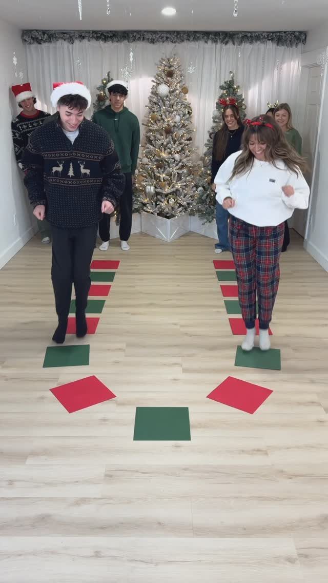 Young adults playing a game on colored floor squares near a Christmas tree.