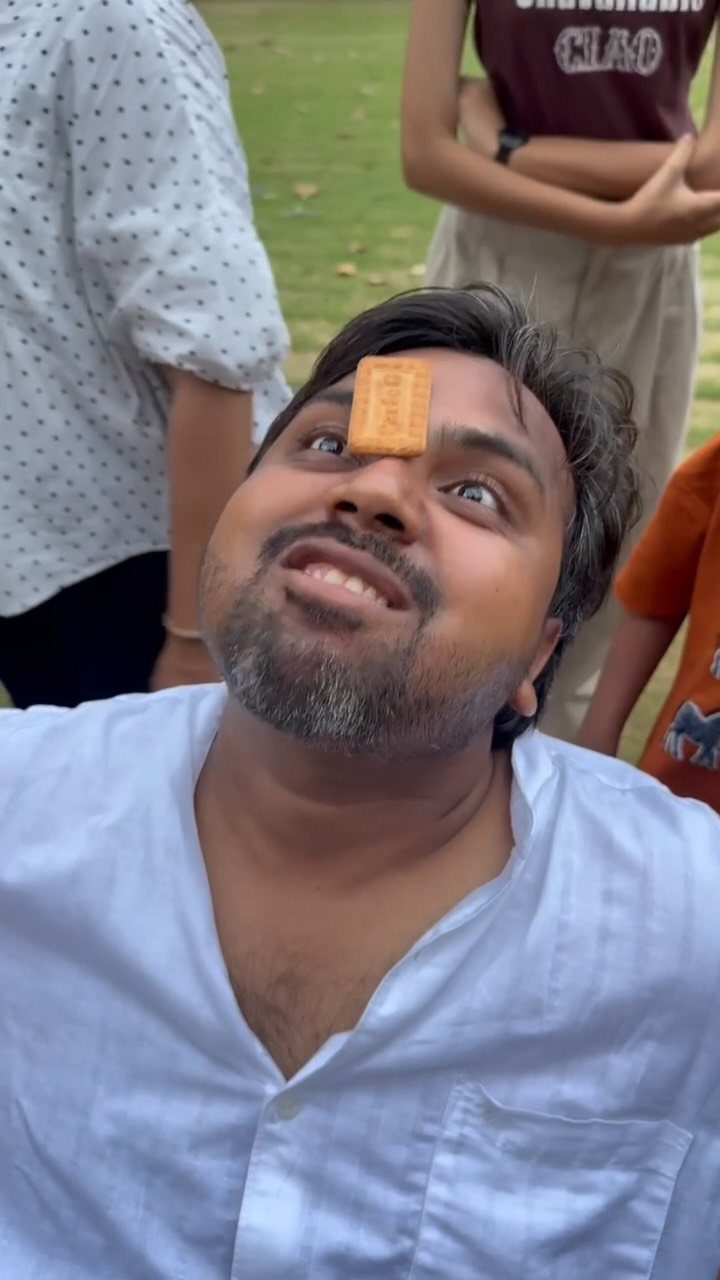 Man lying on grass with a small cracker balanced on his forehead during a game.