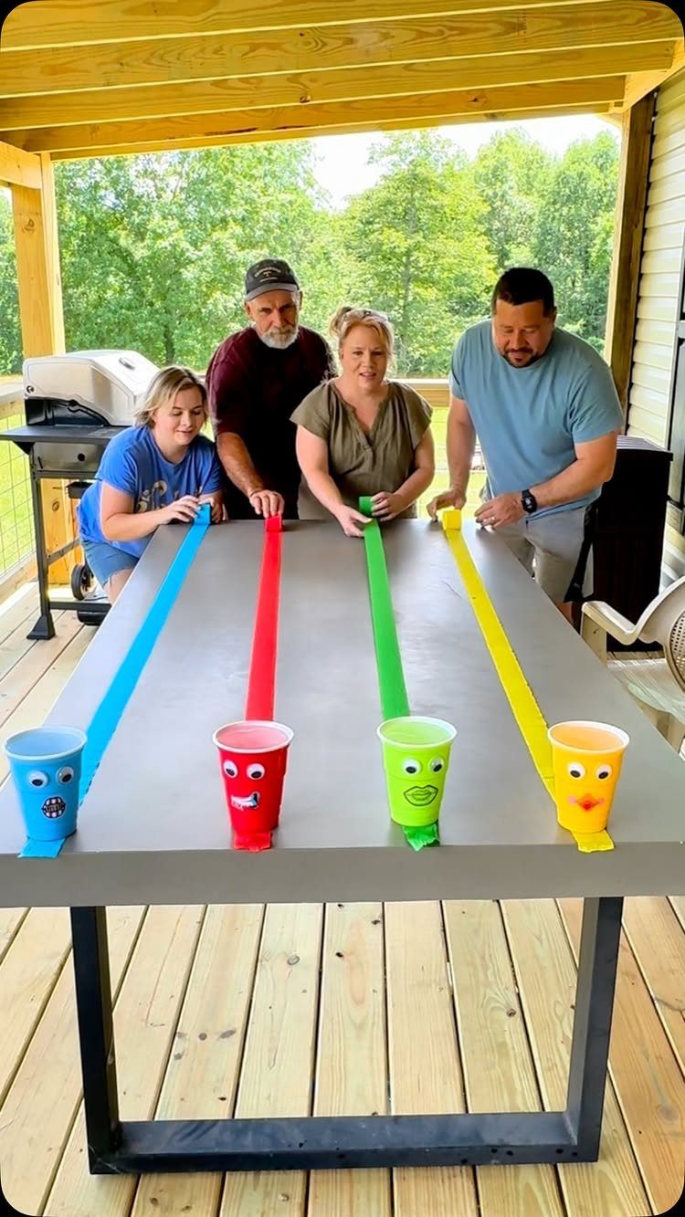 Four adults playing a racing game with colorful paper strips and plastic cups.