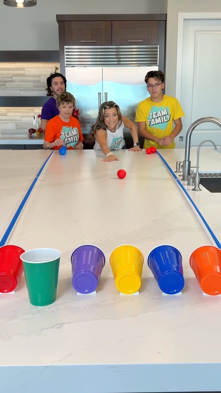 Children playing a game with colorful plastic cups and balls on a kitchen counter
