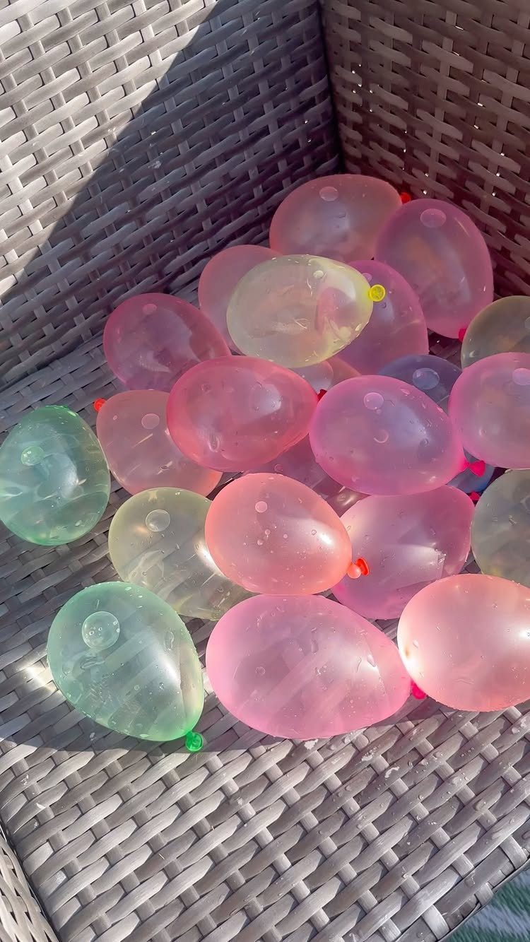 Colorful translucent water balloons filling a grey woven wicker basket outdoors.
