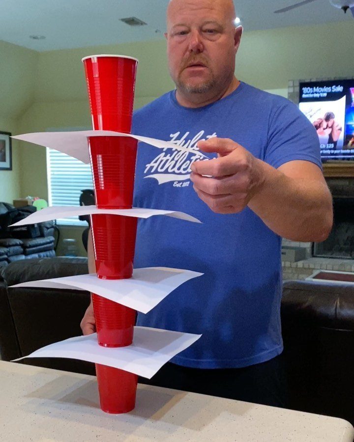 Man pointing at a tower of red plastic cups and white paper sheets.