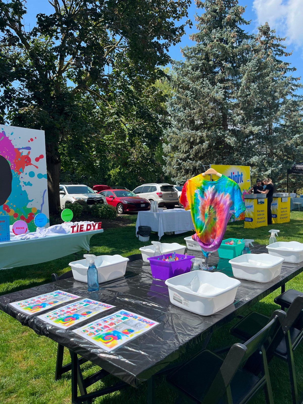 Tie-dye station with white bins and a rainbow shirt outdoors on a lawn