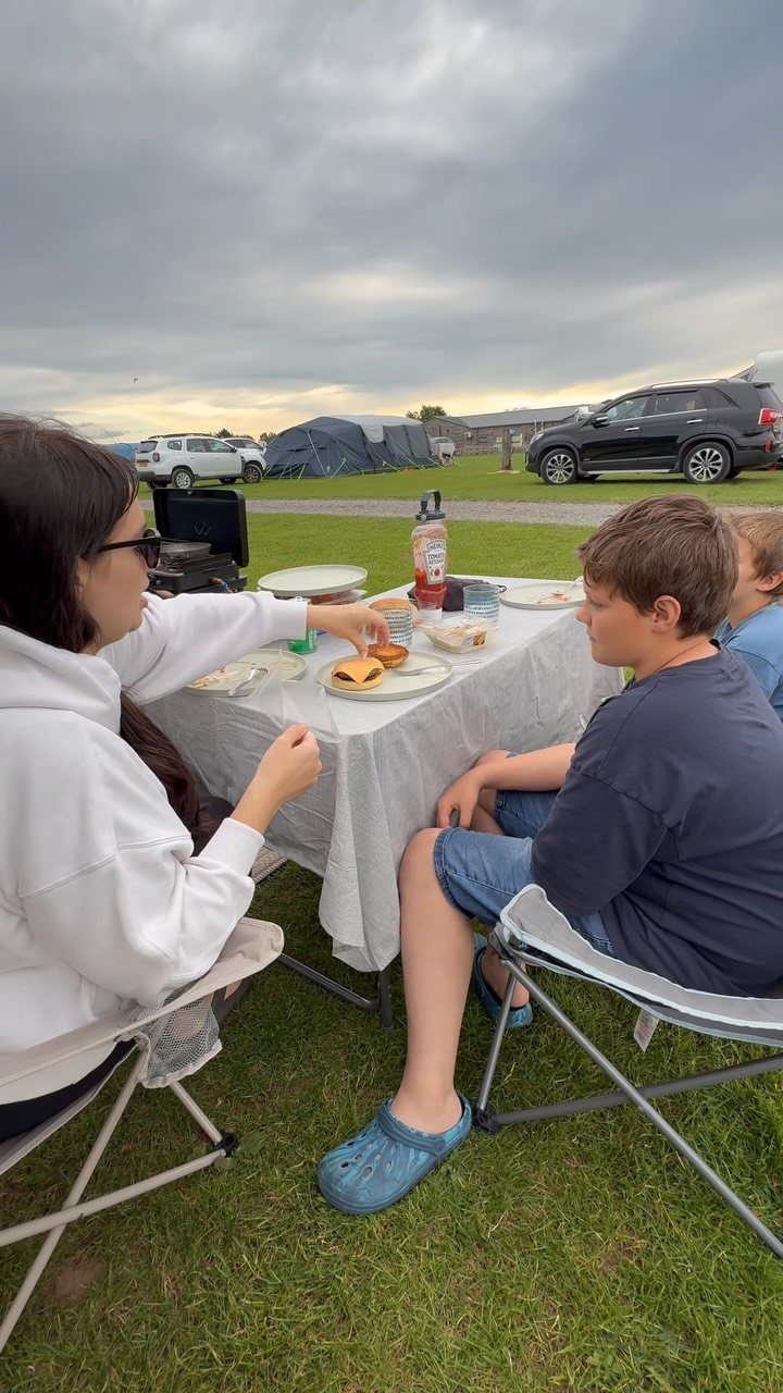People eating burgers at a folding table with a camping tent in background