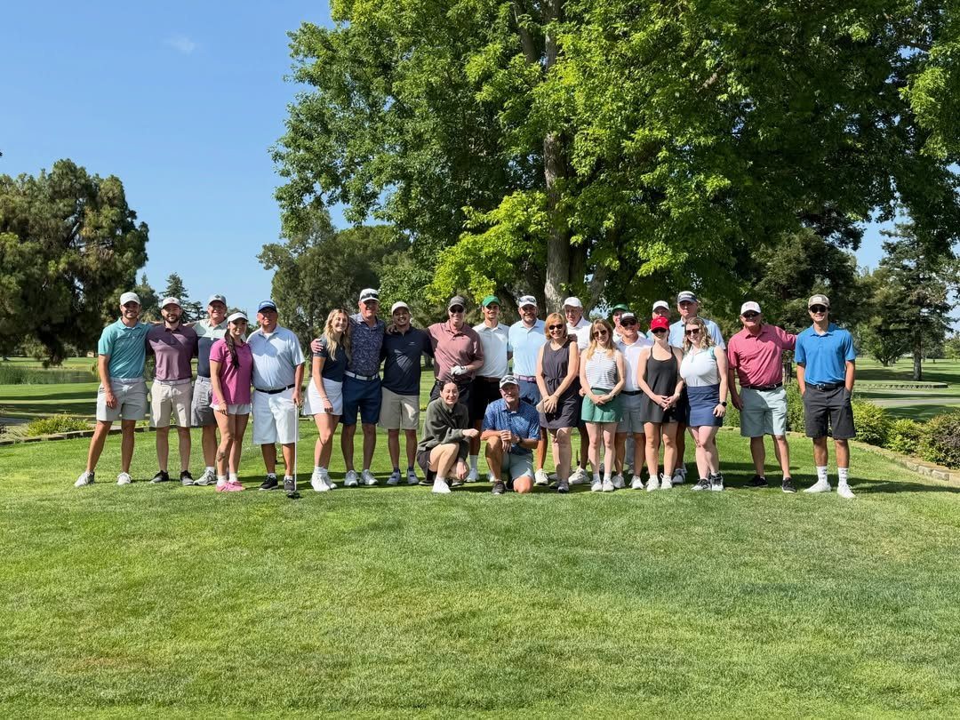 Group of people in golf clothing posing on a green golf course.