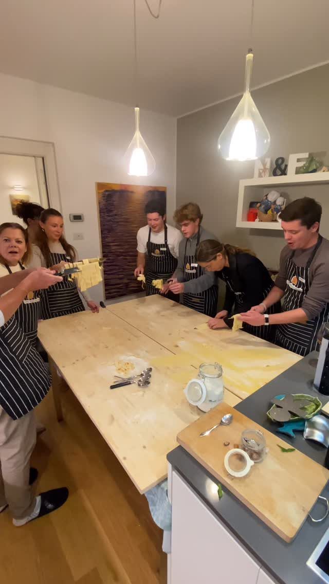 Group of adults in aprons making fresh pasta together around a wooden table