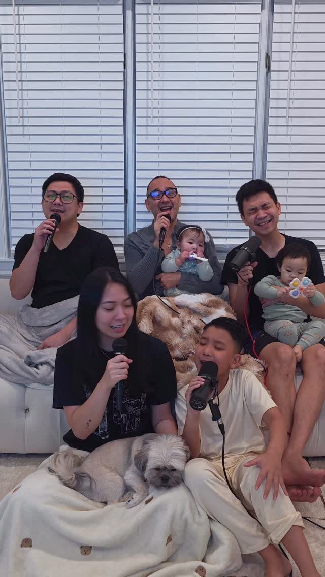 Family members of various ages singing into microphones while relaxing in a living room.