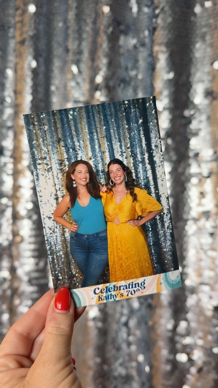 Two women smiling in a photo booth print held against a sequin backdrop.