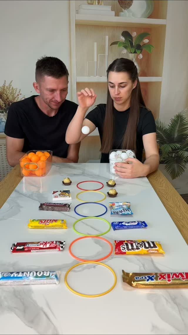 Man and woman playing a ring toss game with candy on a table