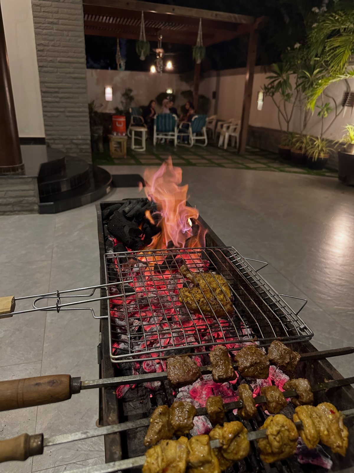 Meat skewers and grilled meat cooking over open flames on an outdoor patio.