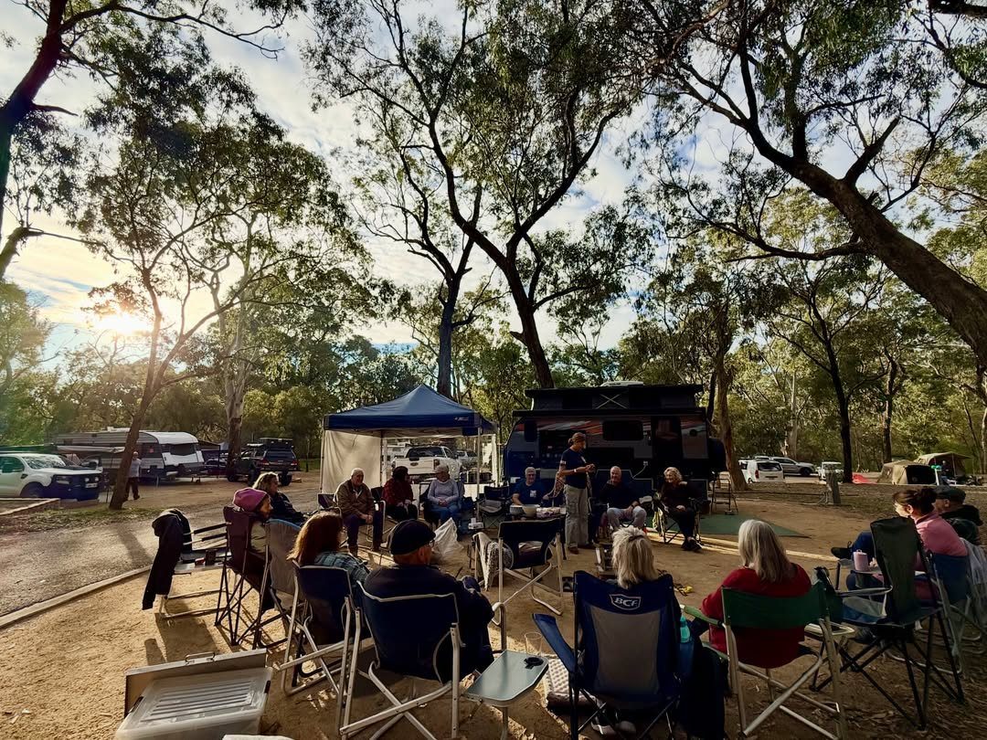 People sitting in folding chairs at a campground with tents and camper trailers.