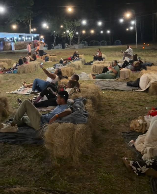 People relaxing on hay bales and blankets under string lights in a field