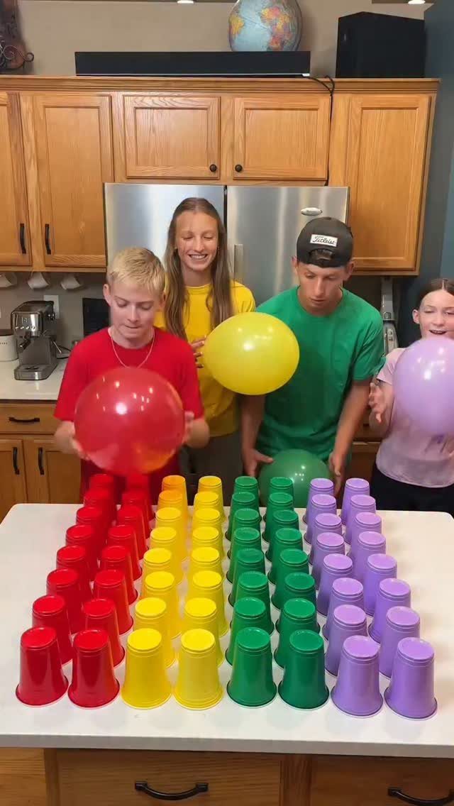 Four children with colorful balloons standing behind a grid of colorful plastic cups.