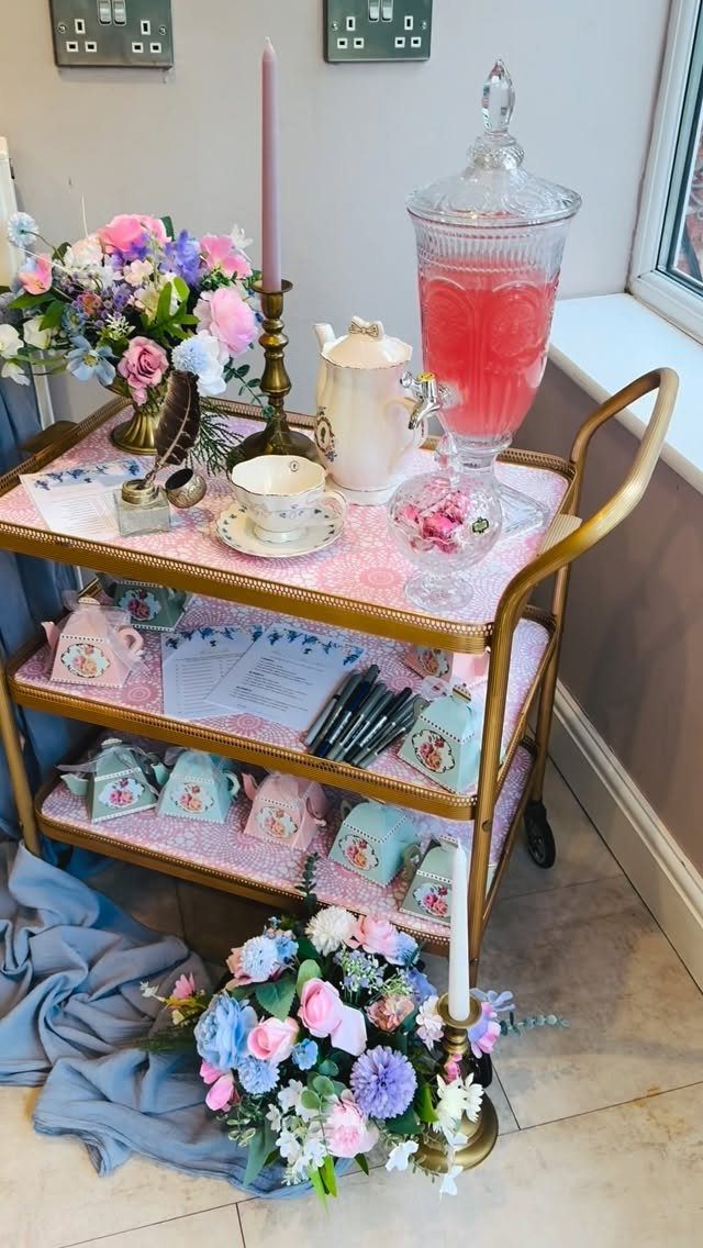 Gold rolling cart decorated with tea sets, pink candles, and pastel floral arrangements.