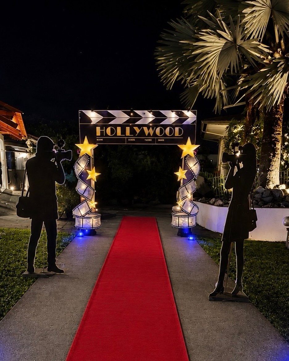 Red carpet entrance with Hollywood clapperboard sign and photographer silhouette cutouts at night.