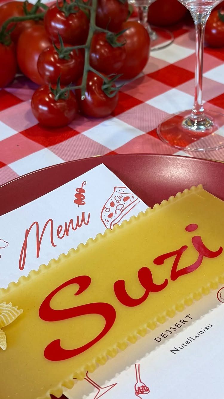 Yellow pasta with red sauce lettering on a red plate with Italian dinner setting