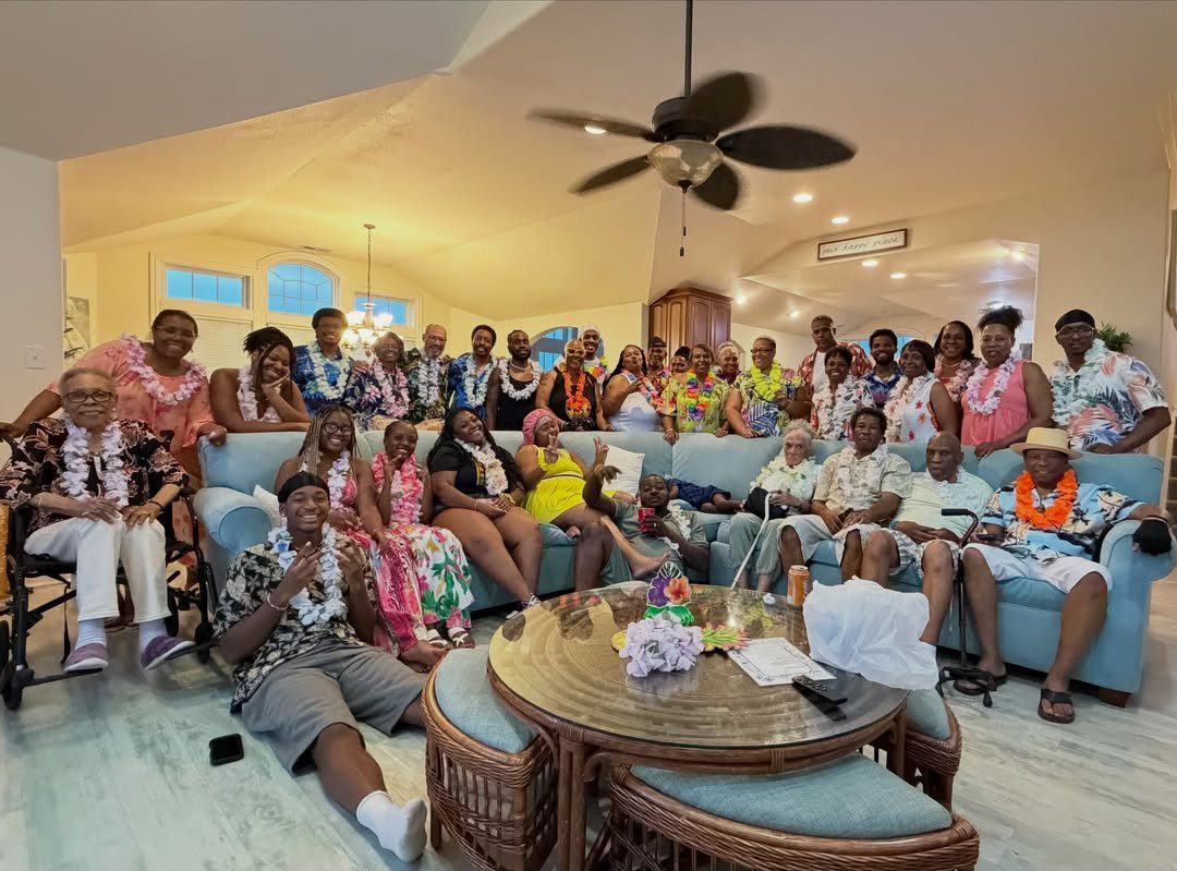 Large family group wearing tropical shirts and floral leis posing in a living room.